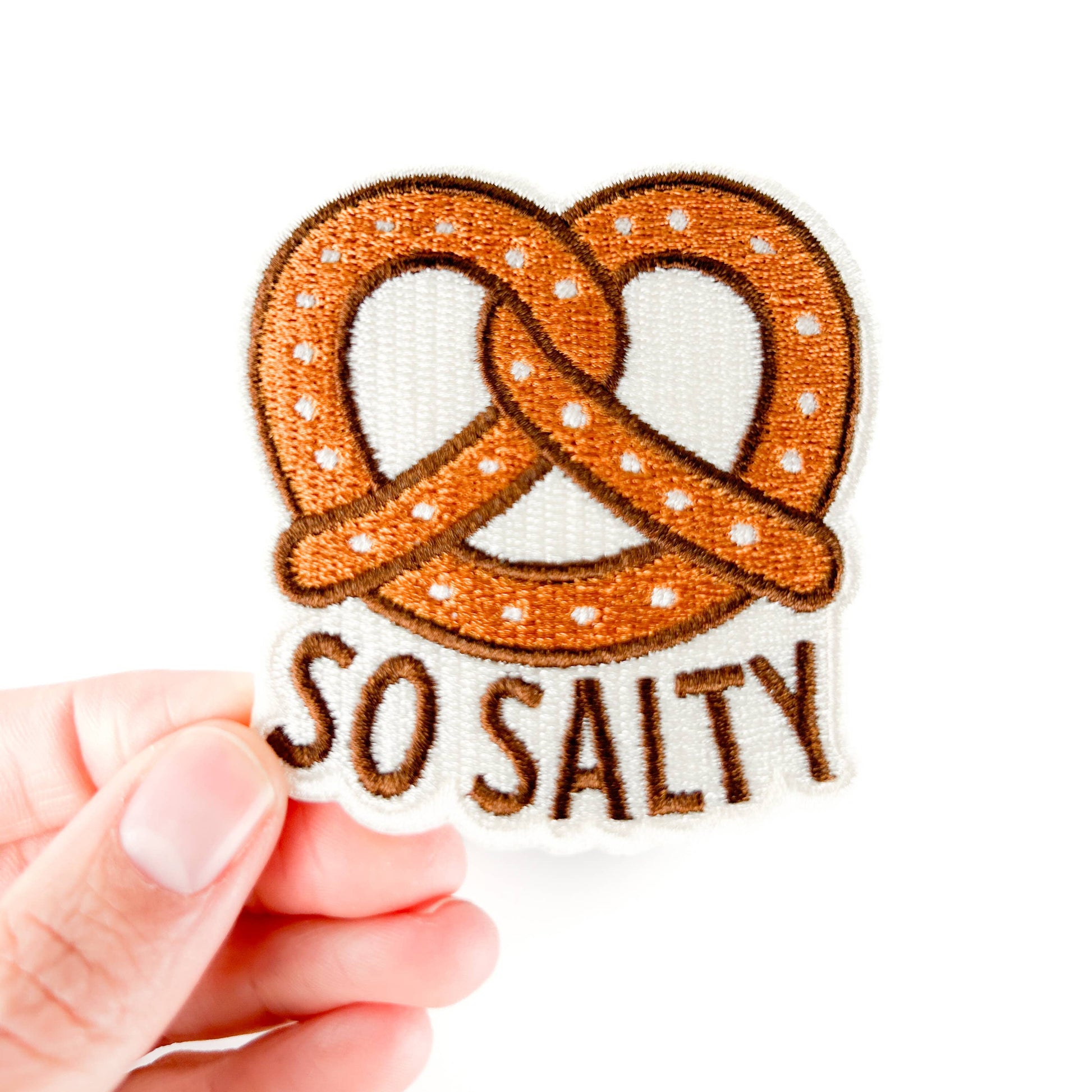 Patches with pretzel design and 'So Salty' text held by a hand on a white background