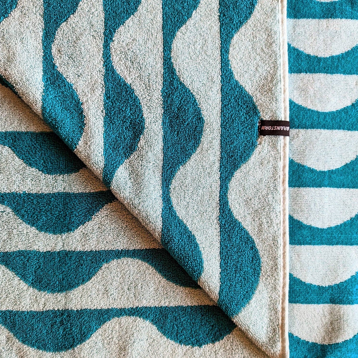 Teal and white wavy patterned fabric with a visible brand label.