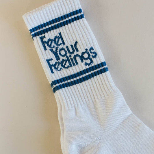 White sock with blue stripes and text 'Feel Your Feelings' on a beige background