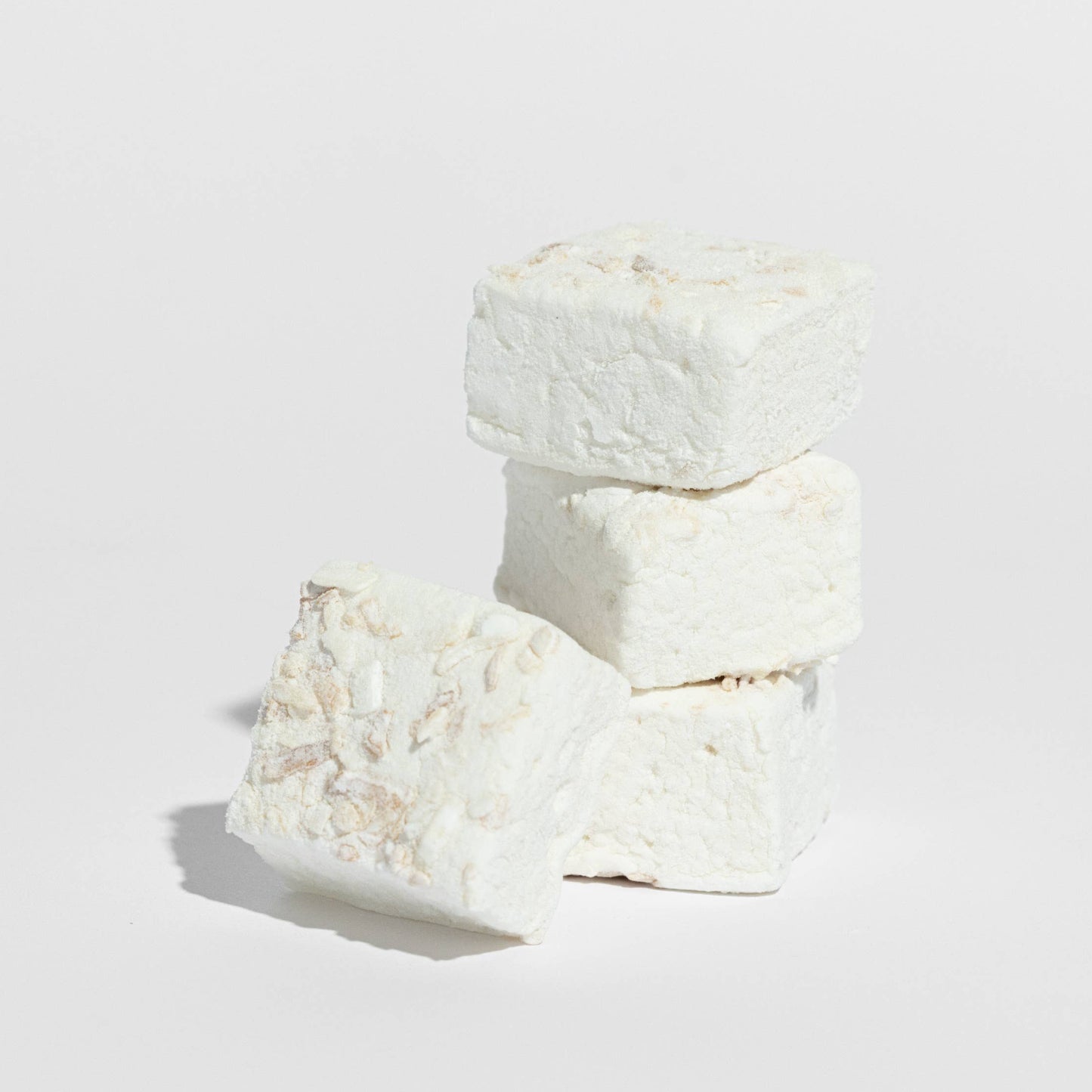 Three white marshmallows stacked on a light gray background