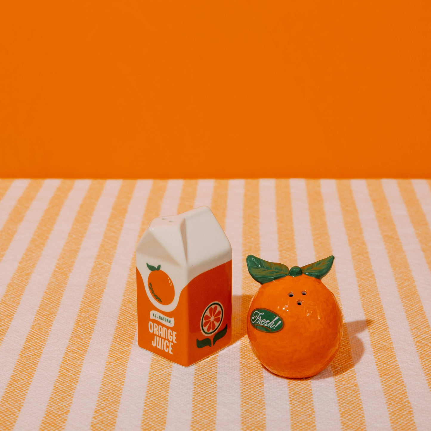 Carton of orange juice and an orange on a striped tablecloth with an orange background