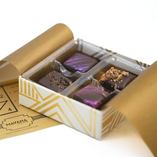 Open box of chocolates with a gold lid and decorative paper, featuring a 'Mayana' brand label.