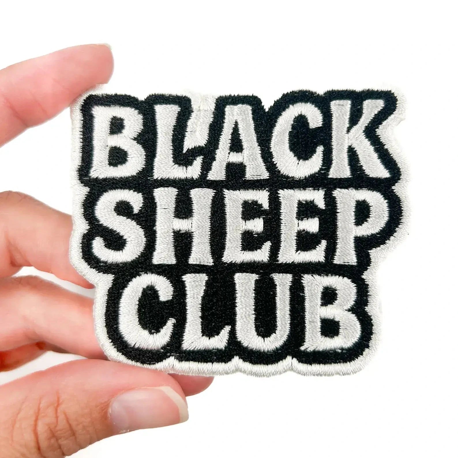 Patch with 'Black Sheep Club' text held by a hand on a white background