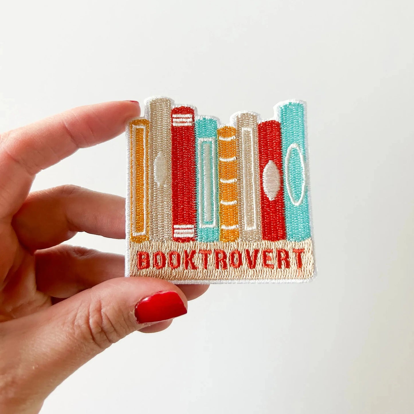 Hand holding a patch with book design and 'BOOKTROVERT' text on a white background
