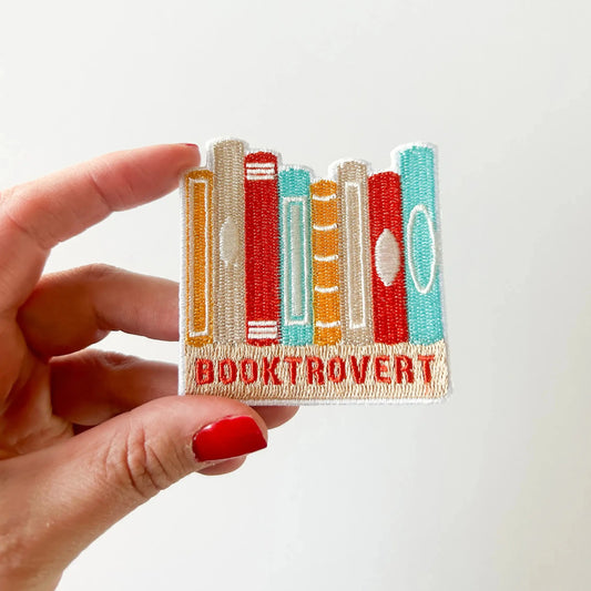 Hand holding a patch with book design and 'BOOKTROVERT' text on a white background