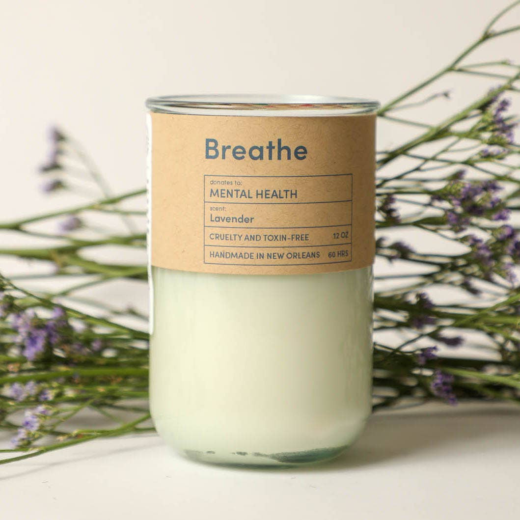 Candle with a 'Breathe' label on a white surface with lavender flowers in the background