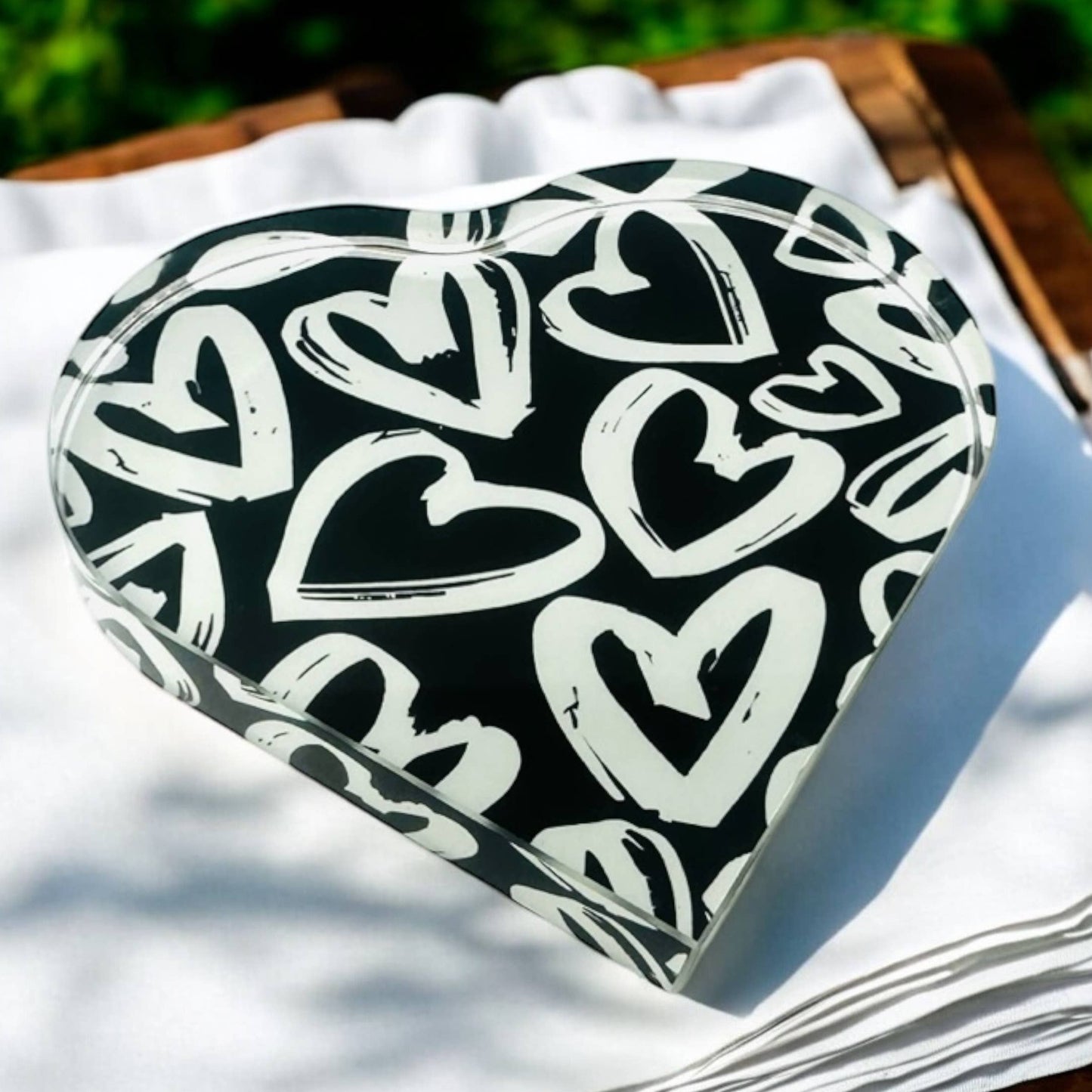 Heart-shaped black and white patterned object on a white surface with greenery in the background