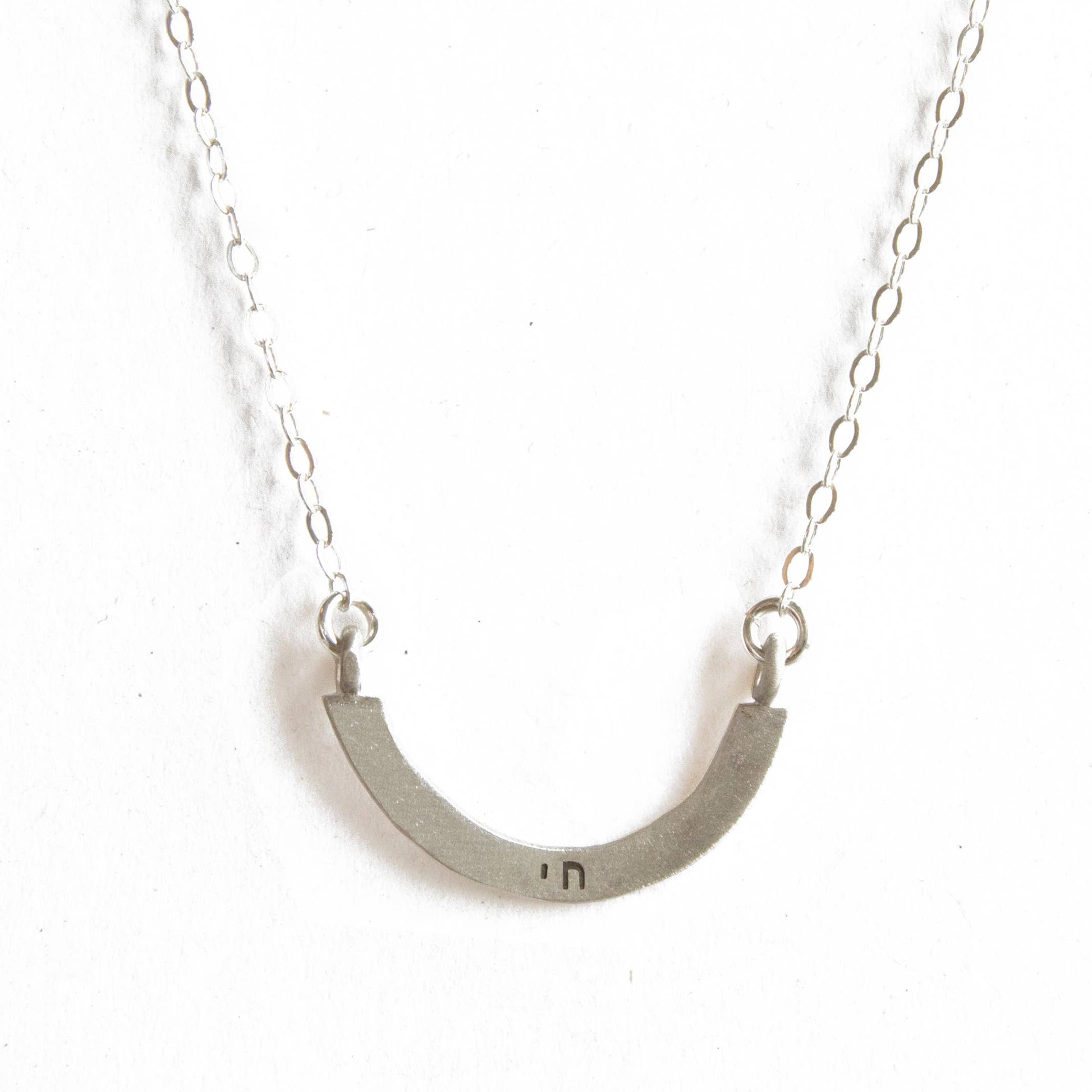 Silver necklace with a curved pendant on a white background
