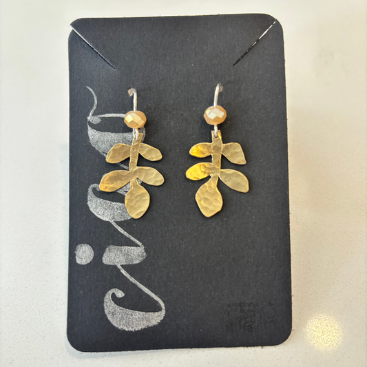 Gold leaf-shaped earrings on a black card with 'Eve' branding.