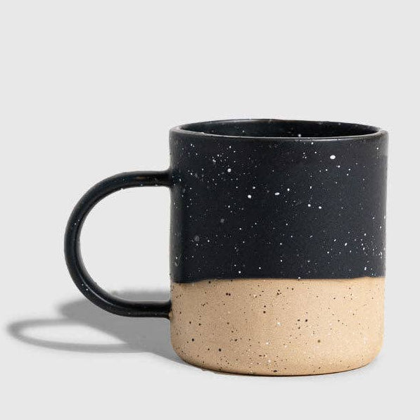 Black speckled mug with beige base on a light gray background