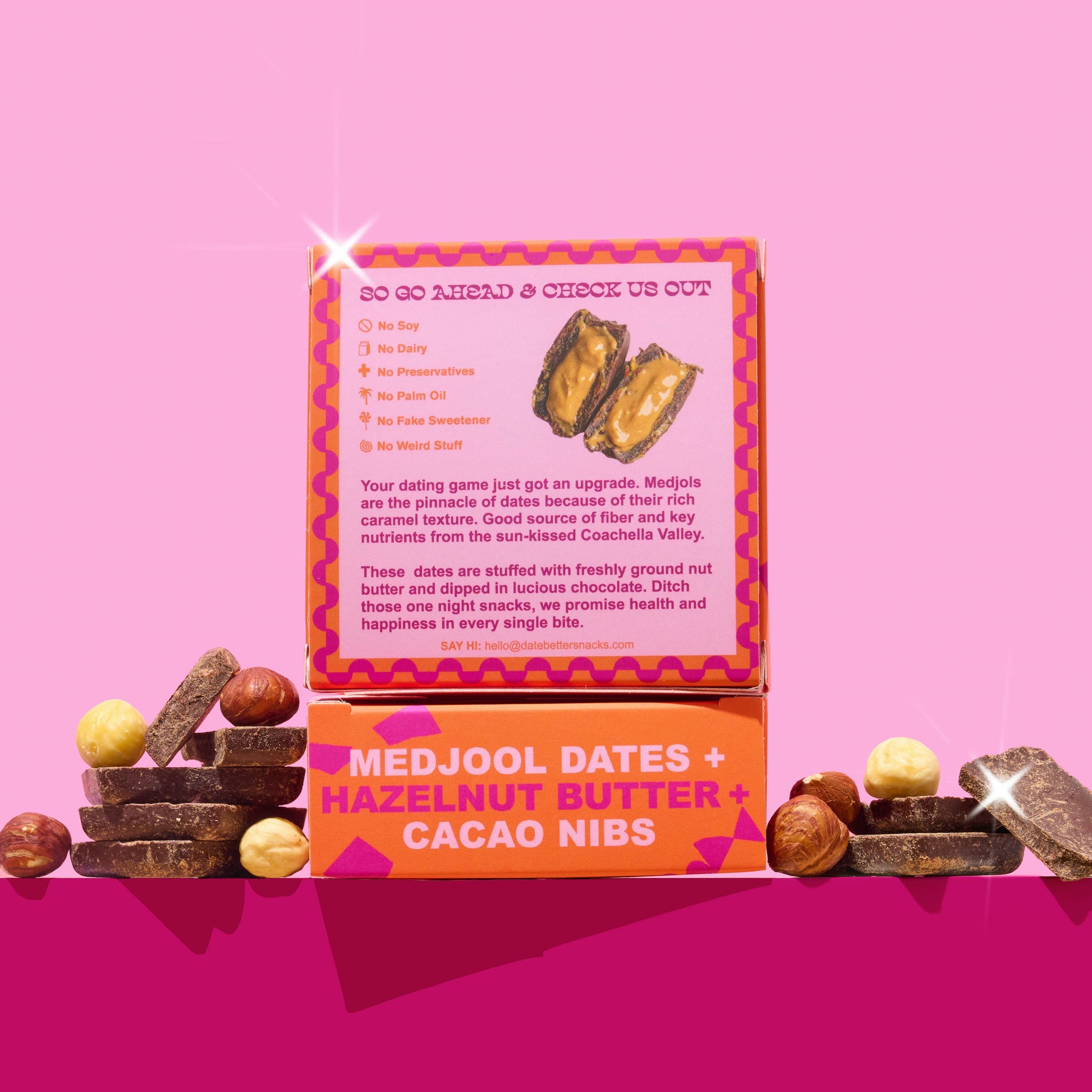Box of Medjool dates, hazelnut butter, and cacao nibs on a pink background