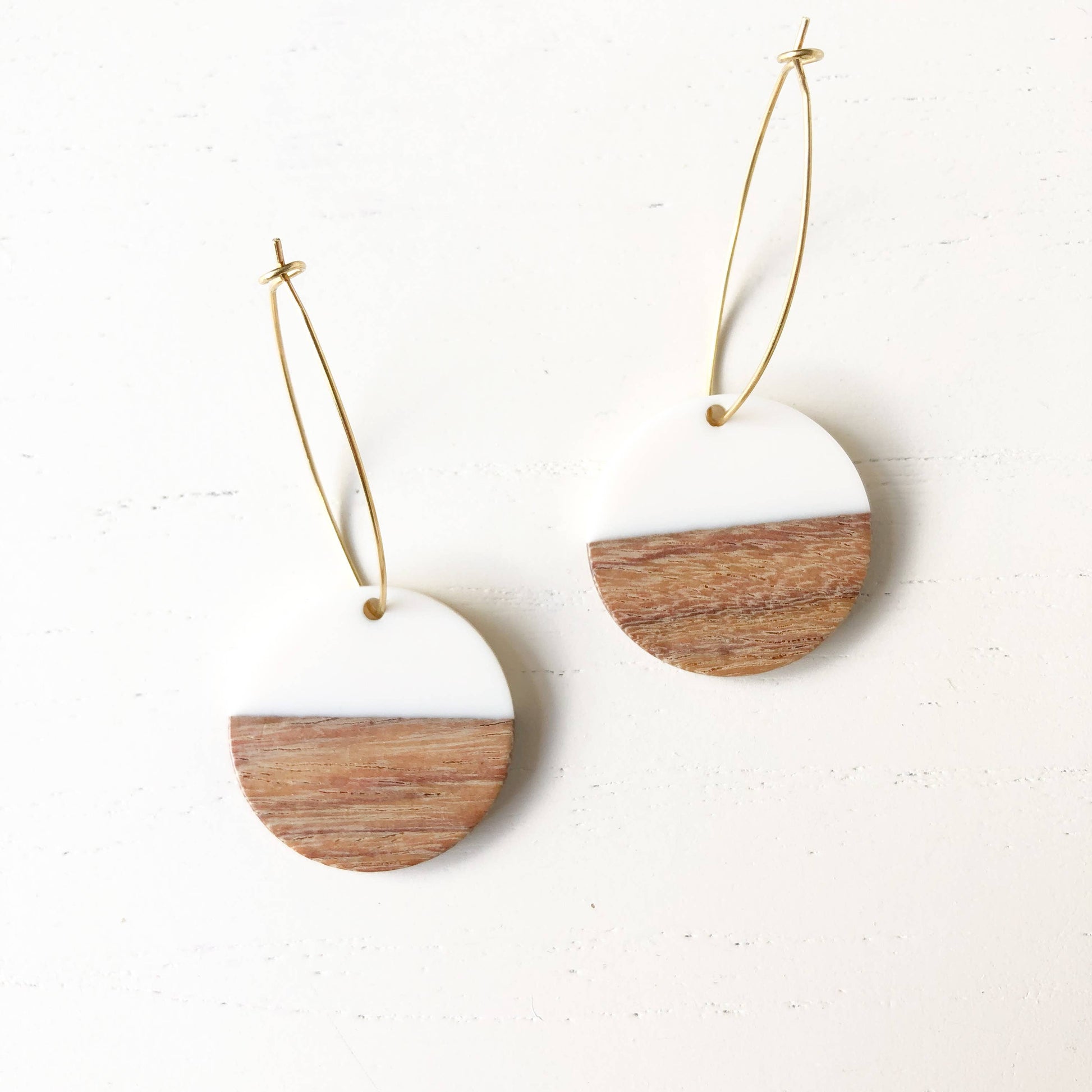Pair of earrings with wooden and white half-circle design on a light background