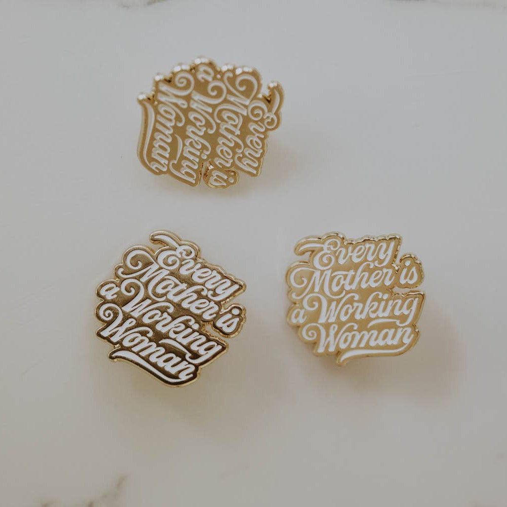 Three gold pins with engraved text on a marble surface