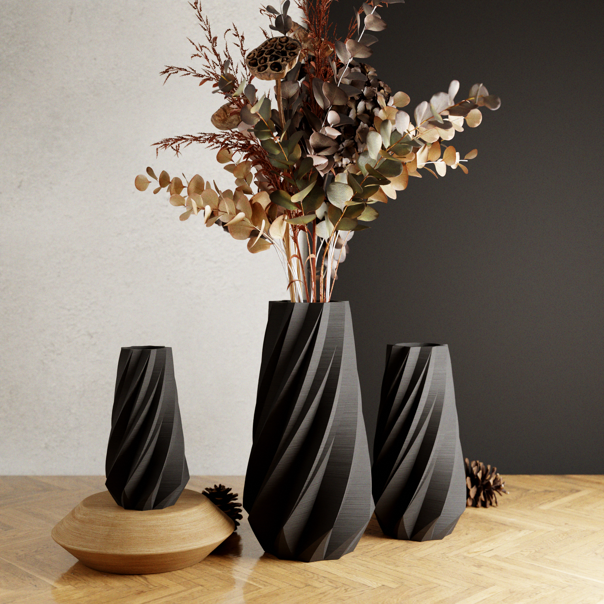 Three black textured vases with a central vase holding dried flowers on a wooden surface.