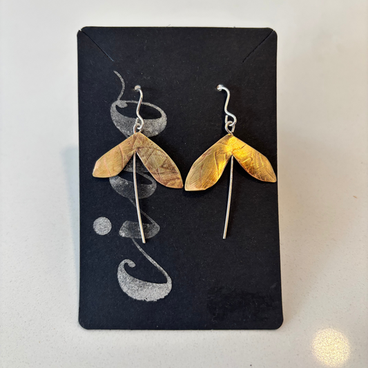 Pair of gold leaf-shaped earrings on a black card with silver designs.