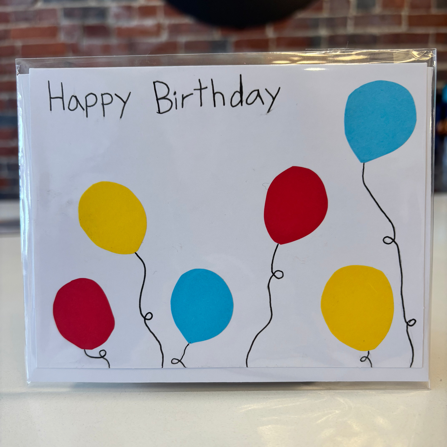 Birthday card with colorful balloons and 'Happy Birthday' text on a white surface.