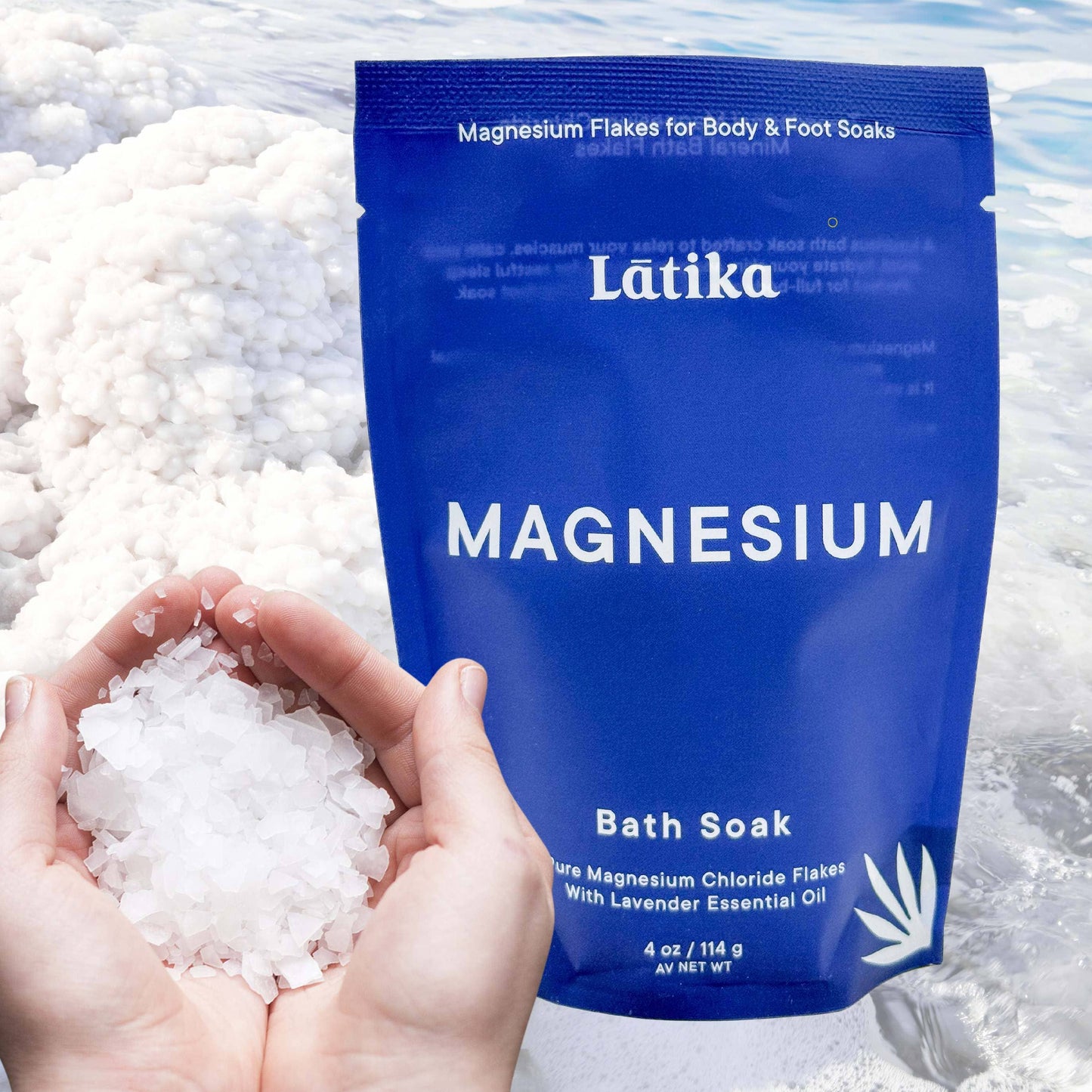 Blue package of Latika Magnesium Bath Soak with magnesium flakes in hands and water background