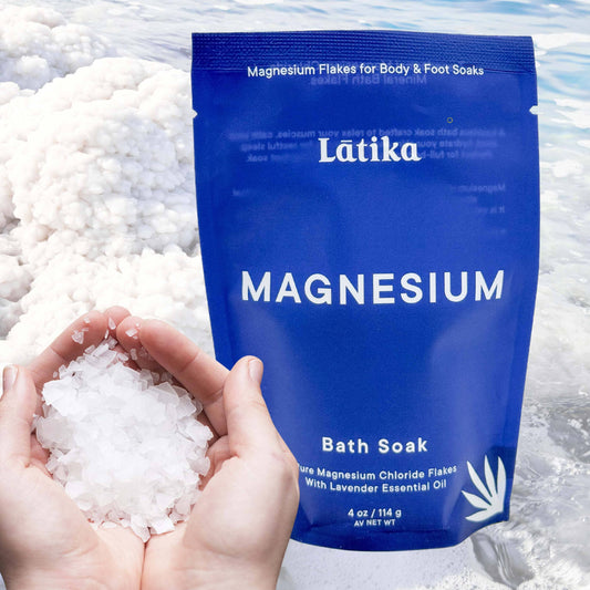 Blue package of Latika Magnesium Bath Soak with magnesium flakes in hands and water background