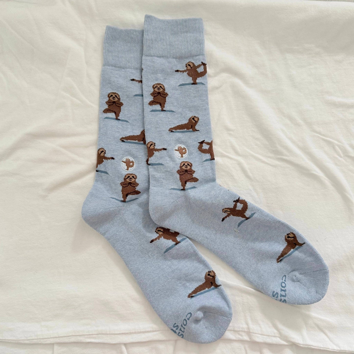 Pair of light blue socks with sloth illustrations on a white fabric background