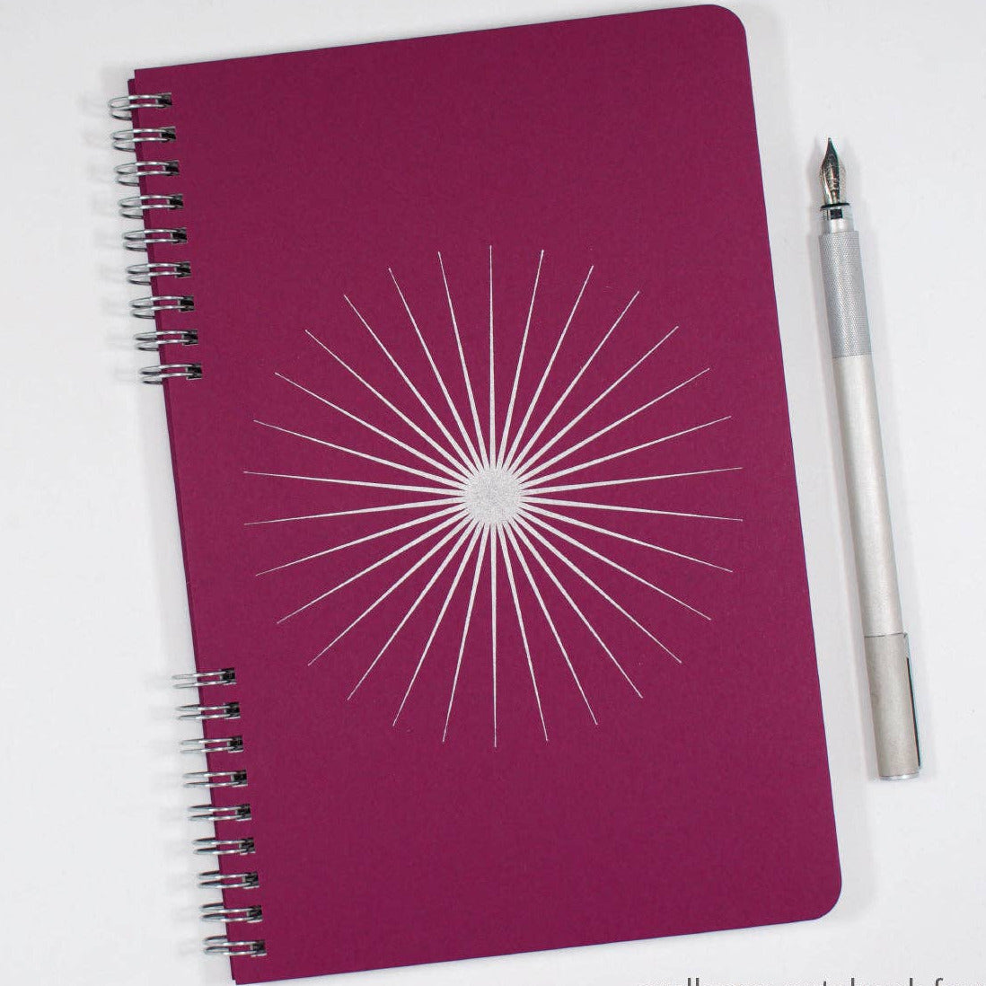 Purple notebook with white starburst design and a pen on a white background