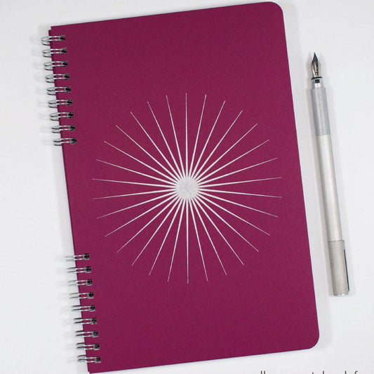 Purple notebook with white starburst design and a pen on a white background