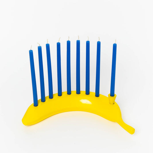 A novelty Hanukkah menorah made from a yellow banana-shaped base holding nine blue candles, photographed on a clean white background.