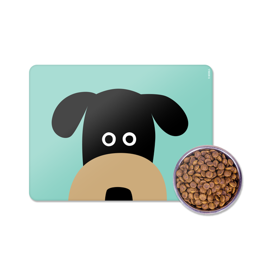 A rectangular pet mat with a stylized black and tan dog face on a light aqua background, shown next to a small round bowl filled with brown kibble on a white studio background.