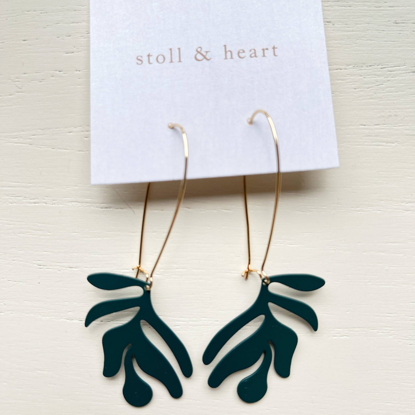 Green leaf-shaped earrings on a 'stoll & heart' card against a light background