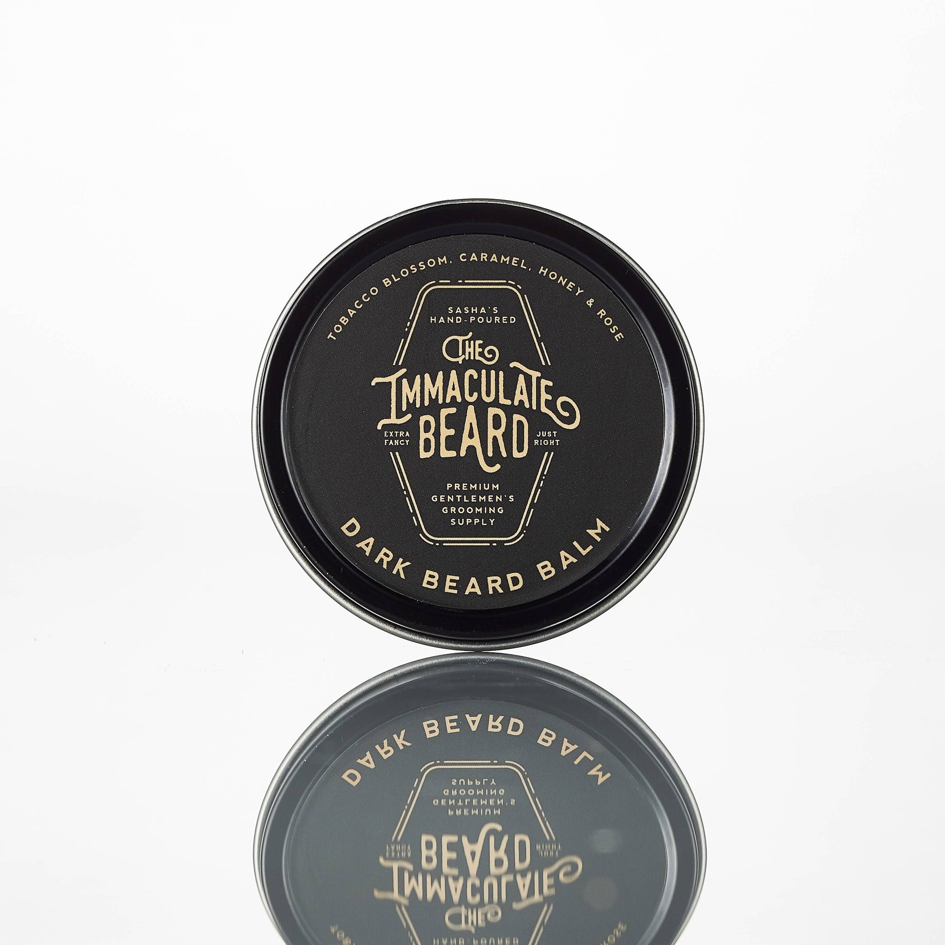 Dark-colored beard balm container with 'The Immaculate Beard' branding on a white background