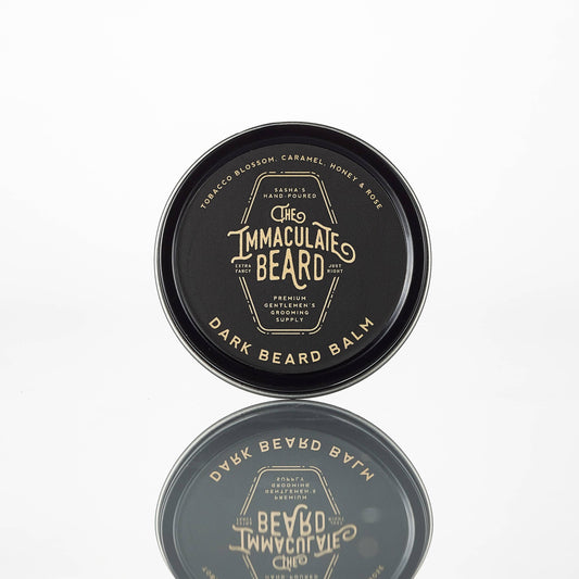 Dark-colored beard balm container with 'The Immaculate Beard' branding on a white background