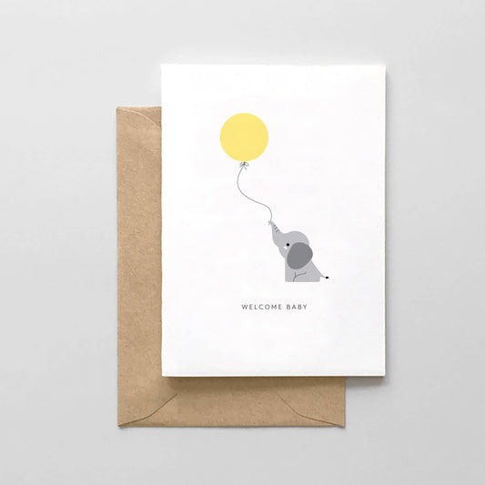 Greeting card with an elephant holding a yellow balloon and 'Welcome Baby' text, accompanied by a brown envelope on a light gray background.