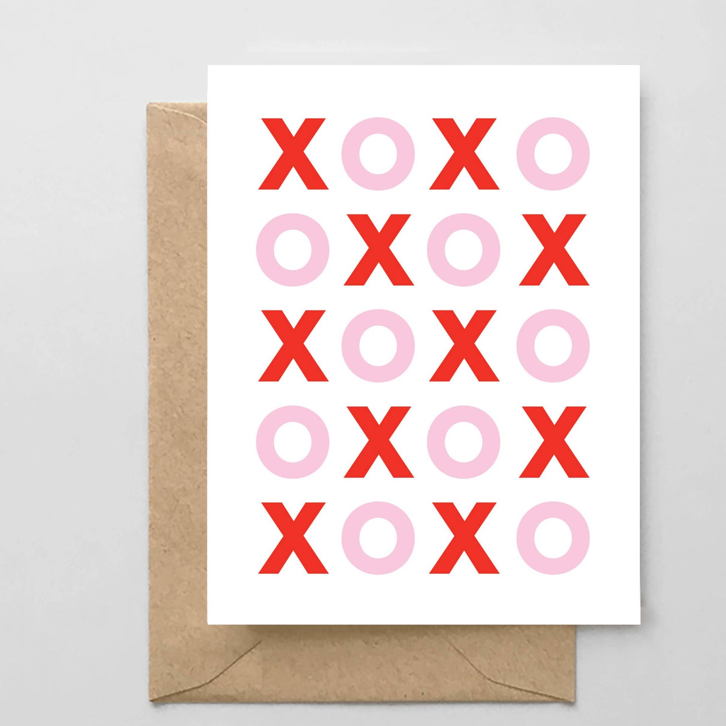 Greeting card with red and pink 'XO' pattern on a white background, accompanied by a brown envelope.