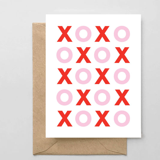 Greeting card with red and pink 'XO' pattern on a white background, accompanied by a brown envelope.